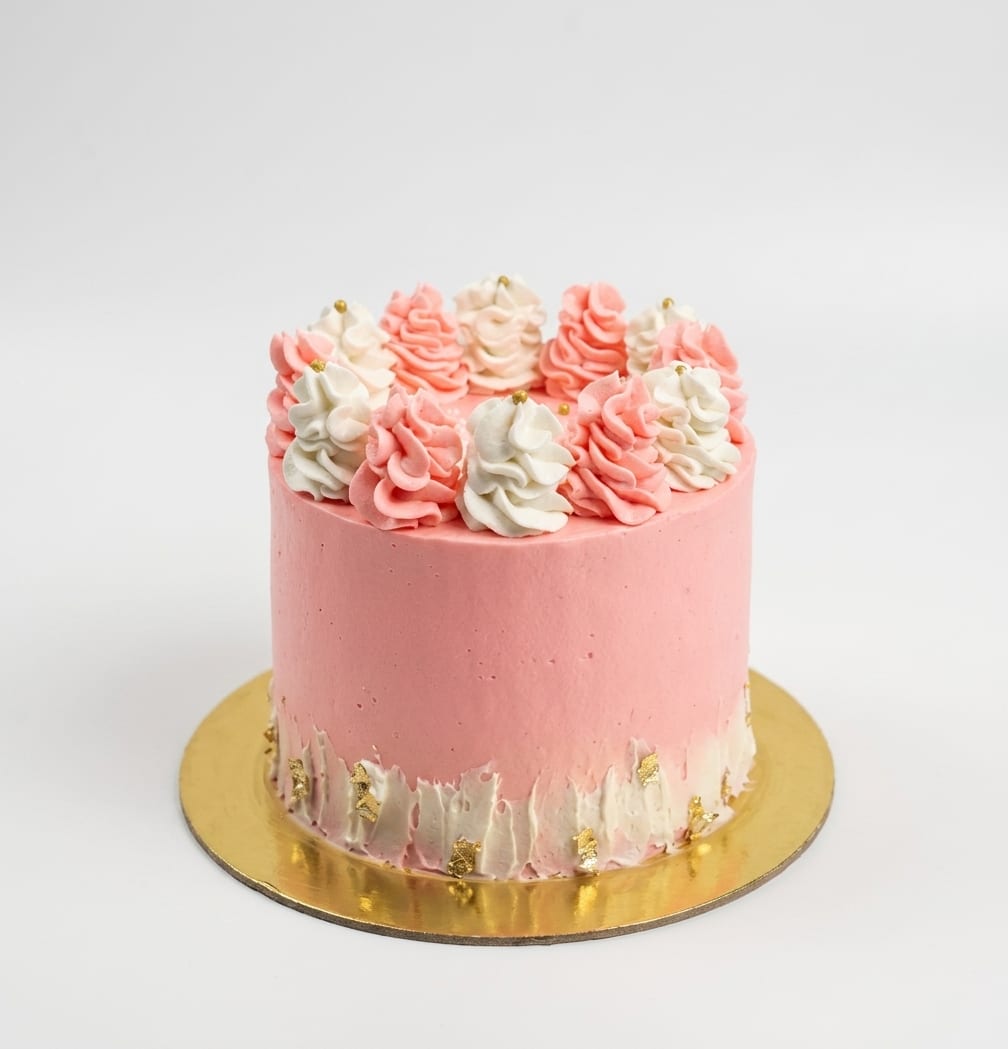 Torta cubierta en buttercream rosa con rosetones rosa y blanco y hojuelas de pan de oro